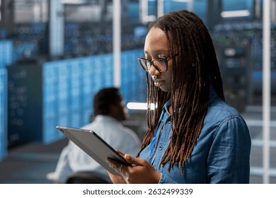 Engineer in server room using tablet to implement and manage data backup solutions to protect against data loss and ensuring efficient recovery processes, identifying and resolving technical issues