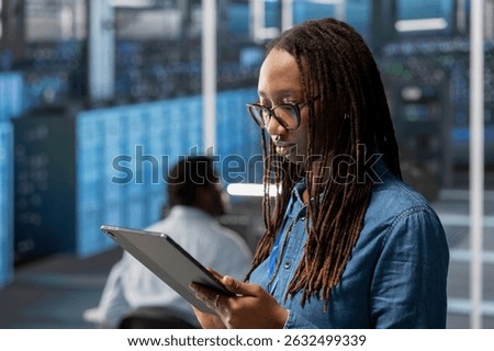 Engineer in server room using tablet to implement and manage data backup solutions to protect against data loss and ensuring efficient recovery processes, identifying and resolving technical issues