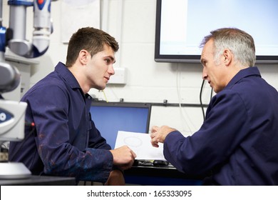 Engineer Showing Trainee Plans With CMM Arm In Foreground