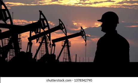 Engineer silhouette in front of oil pumps, red clouds sunset in background