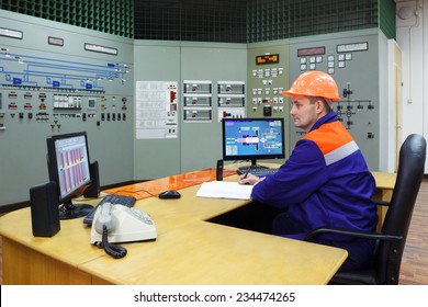 Engineer sitting writes in log on main control panel of gas compressor station 