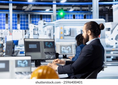 Engineer in solar panel manufacturing facility reviewing photovoltaic system performance on PC. Specialist analyzing production metrics to optimize efficiency in industrial renewable energy plant