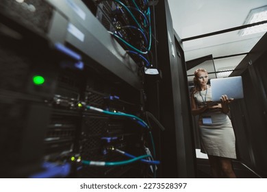 IT engineer standing before working server rack doing routine maintenance check and diagnostics using laptop
