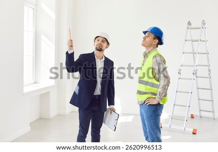 Engineer standing with builder in empty apartment room with ladder in background and pointing at something. Architect or designer consulting foreman in making renovation and design of living space.