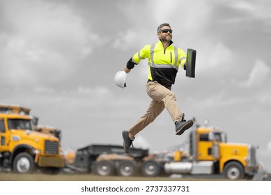 Engineer supervisor running outdoor. Supervisor jumping. Good job. Happy construction builder. Worker jumping at heavy machines. Man engineer running to success. Builder man run to work