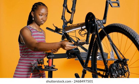 Engineer with tablet in hand analyzing damaged bike over studio background awaiting repair and maintenance. Woman using electronic device to diagnose bicycle on repair stand, camera B