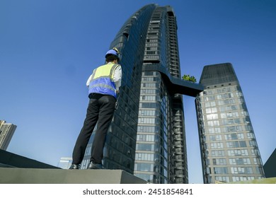 Engineer with tablet on rooftop assessing HVAC system against city skyline, safety equipment and hard hat on.