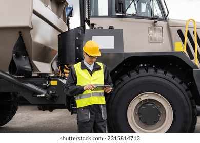 Engineer with tablet stands next to mining truck