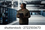 Engineer with tablet walks through data center server rows, implementing advanced power management solutions. IT professional using device to oversee server hub, reducing energy consumption, camera A