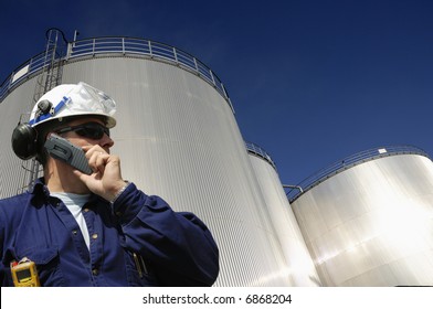 engineer talking in mobile-phone in front of refinery oil tanks