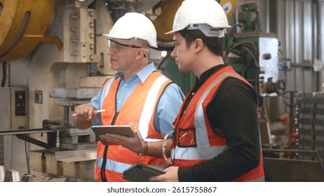 Engineer teaching apprentice to use metal sheet stamping machine, industrial team is working on various projects with tablet computer, worker work together to check the operation system in a factory