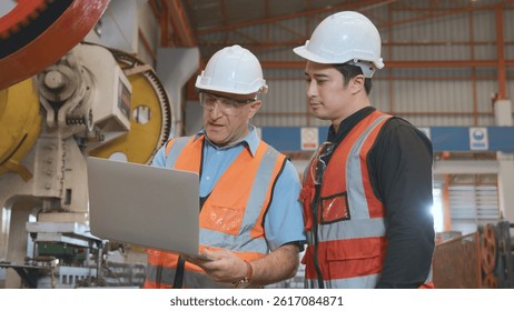 Engineer teaching apprentice to use metal sheet stamping machine, industrial team is working on various projects with laptop computer, worker work together to check the operation system in a factory
