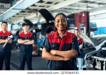 Engineer team checking under car condition on lifter in garage.Young auto mechanic in uniform is looking at camera and smiling examining car.