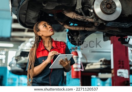 Engineer team checking under car condition on lifter in garage.Young auto mechanic in uniform is looking at camera and smiling examining car.