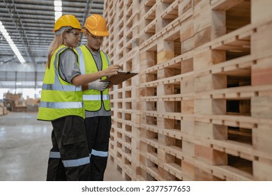 Engineer team standing walking in warehouse examining hardwood material for wood furniture production. Technician man and woman working on quality control in lumber pallet factory. Worker check stock