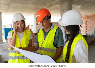 Engineer team studies blueprint while woman uses phone beside supervisor. Foreman points detail and assigns task steps before work starts