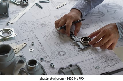 エンジニア技術者が機械部品工学エンジンの図面を設計する製造工場産業産業プロジェクトの青写真で、キャリパー工具を測定