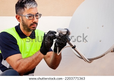 Engineer or technician hispanic repairing or installing a parabolic dish television antenna