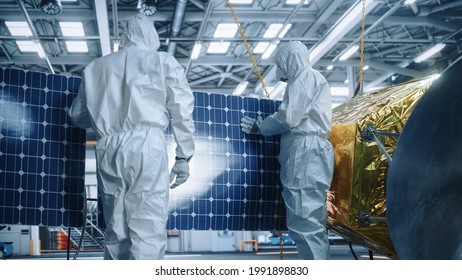 Engineer And Technician In Protective Suits Working On Satellite Construction. Aerospace Agency: Team Of Scientists Fixing Solar Panel Wings To Spacecraft. International Space Exploration Mission