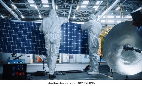 Engineer And Technician In Protective Suits Working On Satellite Construction. Aerospace Agency: Team Of Scientists Fixing Solar Panel Wings To Spacecraft. International Space Exploration Mission