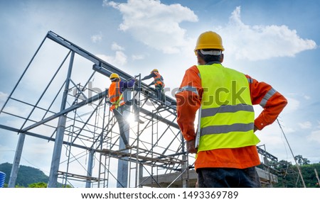 Engineer technician watching team of workers on high steel platform,Engineer technician Looking Up and Analyzing an Unfinished Construction Project.