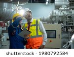 Engineer with technician working with tablet in electrical room of large industry factory.