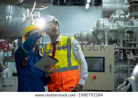 Engineer with technician working with tablet in electrical room of large industry factory.