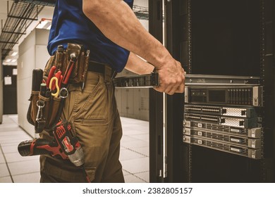 IT Engineer with a tool belt is pulling the server out out of the cabinet in the large data center