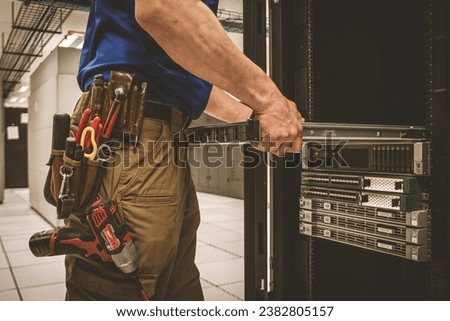 IT Engineer with a tool belt is pulling the server out out of the cabinet in the large data center