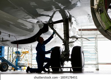 Engineer in uniform inspecting the landing gear of a passenger jet at a hangar. - Powered by Shutterstock