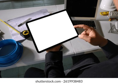 Engineer using digital tablet at construction planning desk with tools and blueprints
