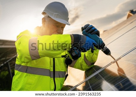 Engineer using a drill for solar panel installation at sunrise. Alternative energy ecological concept image.