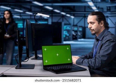 Engineer using green screen laptop to do maintenance in server hub, extending equipment life span. Employee monitoring data center mainframes with mockup notebook for overheating problems
