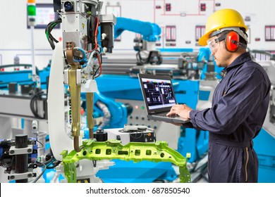 Engineer using laptop computer maintenance automatic robotic hand machine tool in automotive industry manufacturing factory