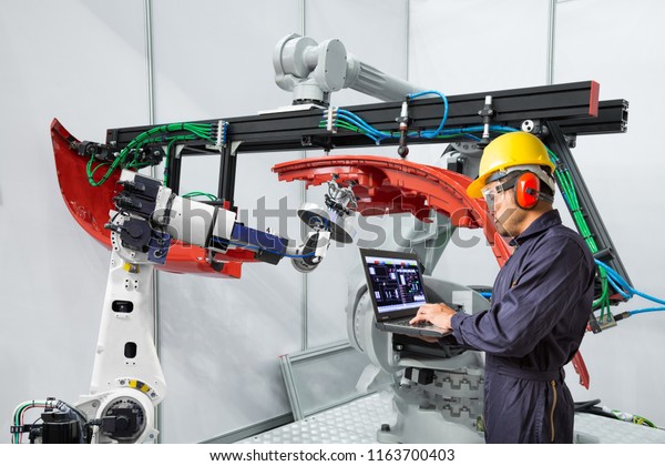 Engineer using laptop computer\
maintenance robot grip automotive workpiece, Smart factory\
concept