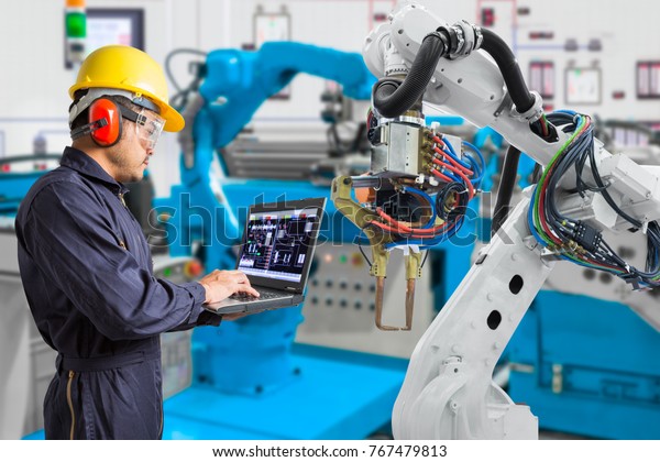 Engineer using laptop computer maintenance\
automatic robotic hand machine tool in automotive industry,\
Industry 4.0 concept