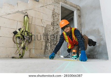 Engineer using laser level to measure floor alignment in construction site with safety gear and tools
