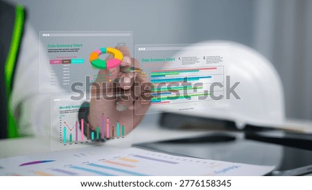 Engineer using pen to analyze holographic data summary charts in office. Professional construction worker reviewing monthly project analysis for growth and industrial management.
