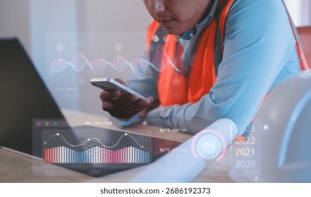 Engineer using smartphone and computer with futuristic charts interface for automation and monitoring Futuristic industrial automation, smart factory technology, monitoring innovation concept