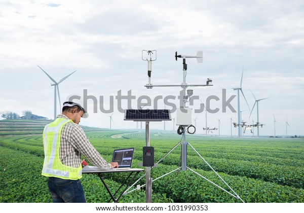 Engineer using tablet computer collect data with\
meteorological instrument to measure the wind speed, temperature\
and humidity and solar cell system on green tea field, Smart\
agriculture concept