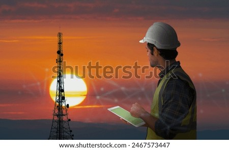 Engineer using tablet to inspect telecommunications tower during sunset, highlighting technology and infrastructure development.