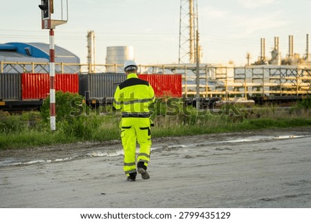 Engineer walking and working on laptop at industrial oil refinery railyard, Industrial inspector using computer at oil and gas refinery logistics site, Worker monitoring operations at railway terminal