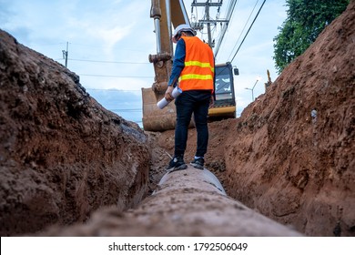 Engineer wear safety uniform examining excavation concrete Drainage Pipe and manhole water system underground at construction site. - Shutterstock ID 1792506049