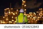 Engineer wear uniform and helmet stand workplace hand holding tablet computer, survey inspection teamwork plant site to work with night lights oil refinery background.