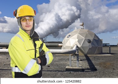 Engineer, Wearing All Necessary Safety Gear, Standing In Front Of A Futuristic Dome, A Part Of A Geothermal And Sustainable Energy Plant In Iceland