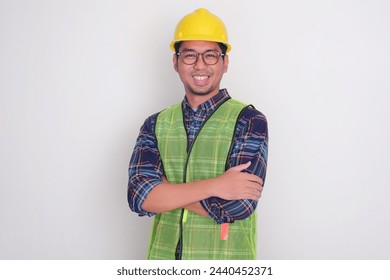 An engineer wearing hard hat and vest smiling with arms crossed - Powered by Shutterstock