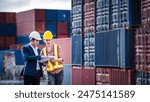 Engineer wearing a hardhat standing cargo at the container yard and check for control loading Containers box from Cargo freight ship for import and export. Teamwork concept