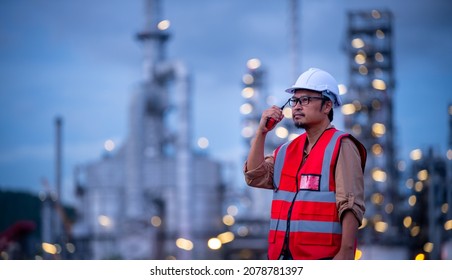 Engineer wearing safety uniform and helmet looking with radio communication conversation checking and inspection by oil refinery factory at night time background. - Shutterstock ID 2078781397