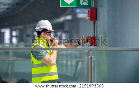 Engineer wearing safety uniform and helmet under checking fire evacuation alarm emergency system in industry factory and exit door is factory security protection concept.