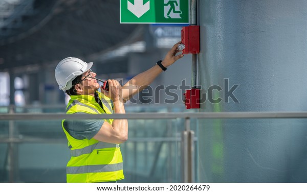 Engineer wearing safety\
unifrom and helmet under checking fire alarm emergency system in\
industry factory and exit door is factory security protection\
concept.
